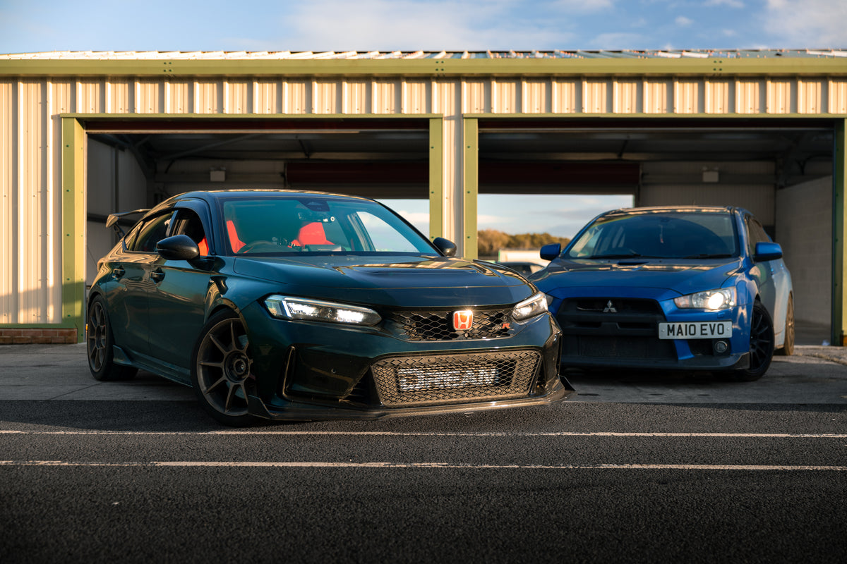 Two cars parked in front of a garage with a clear sky.